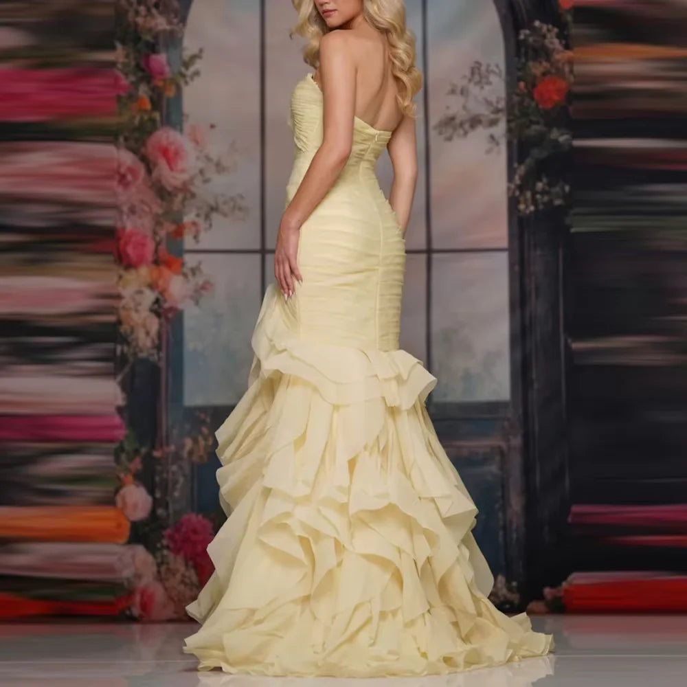 Woman wearing a pale yellow strapless mermaid gown with tiered ruffles by Dream Designs Boutique