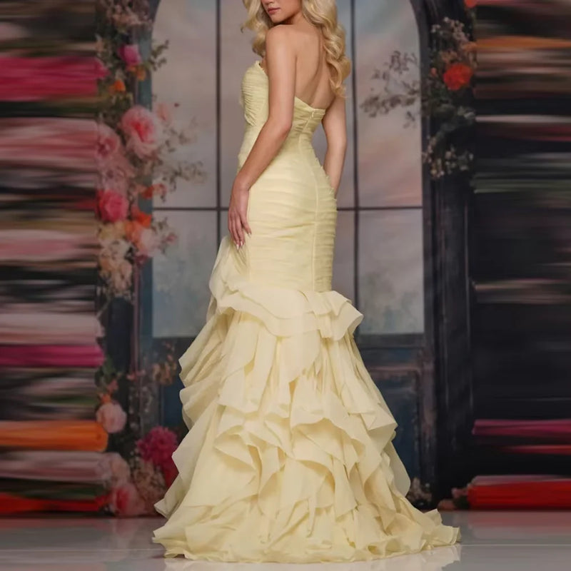 Woman wearing a pale yellow strapless mermaid gown with tiered ruffles by Dream Designs Boutique